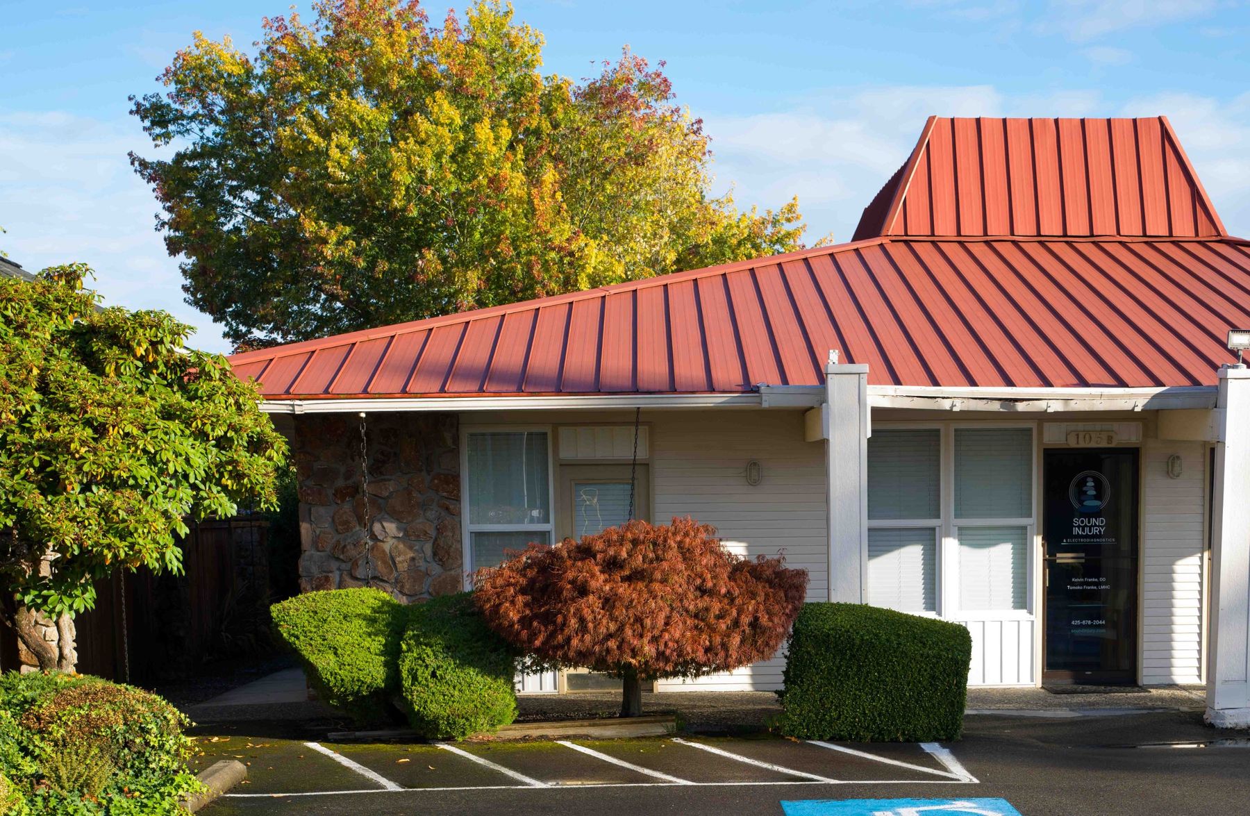 The Edmonds building from the parking lot: a single-story building with a red metal roof and a stone column, with the Suite B-105 door at the right end